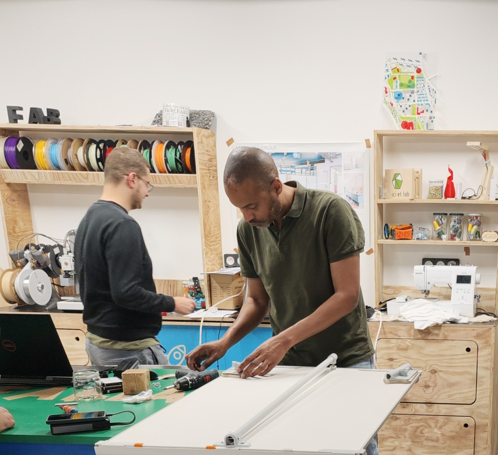 Deux personnes travailles au fablab de l'AGECA sur le plan de travail.